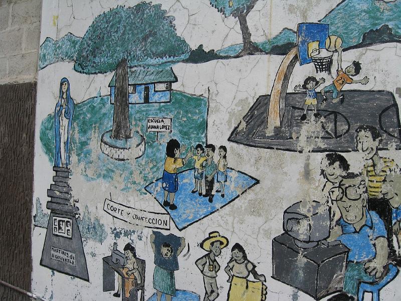 MK014.jpg - Mural in front of the El Despertar Center shows statue of Virgin Mary on pedestal in memory of Martyrs of El Despertar, and current activities of classes, eye testing, weddings and dancing, basketball.